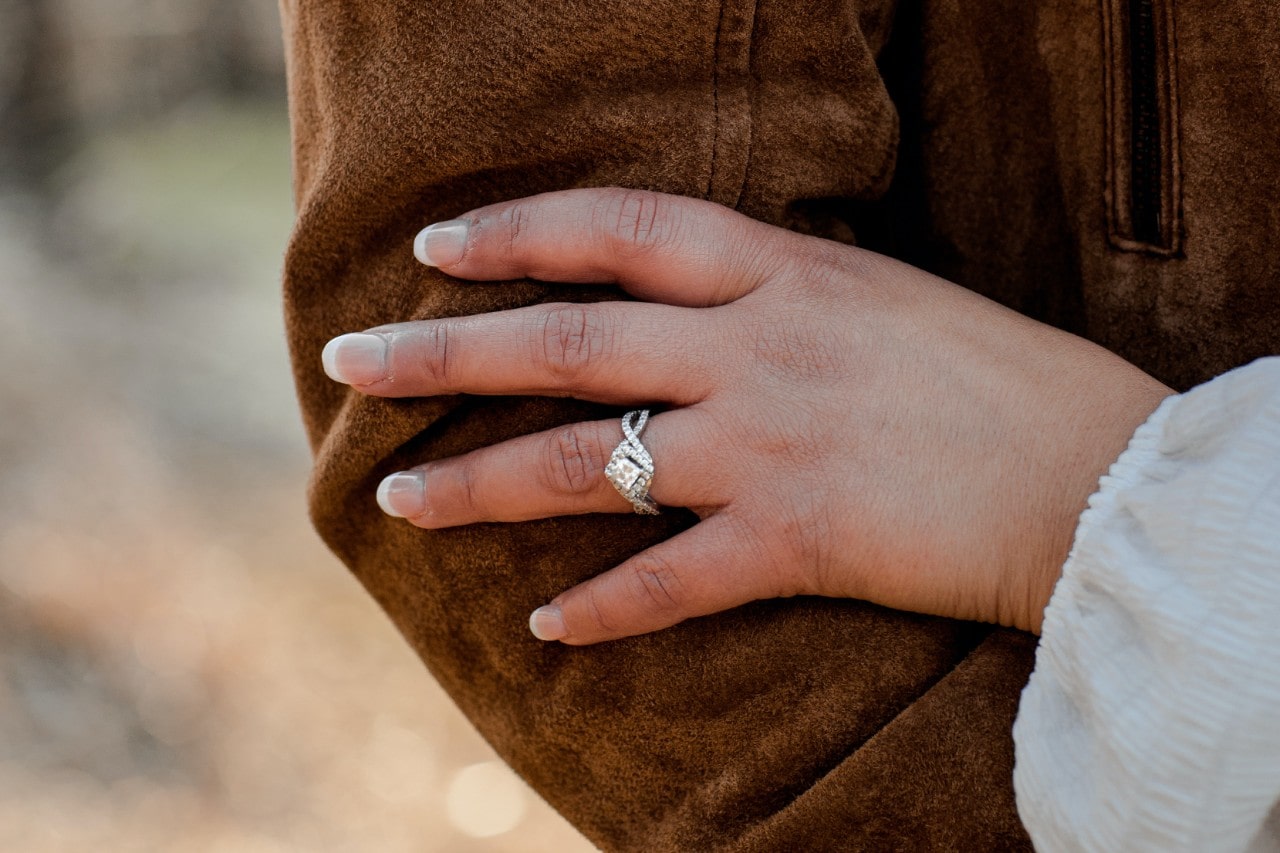 A woman’s hand resting on a man’s arm, wearing a silver engagement ring