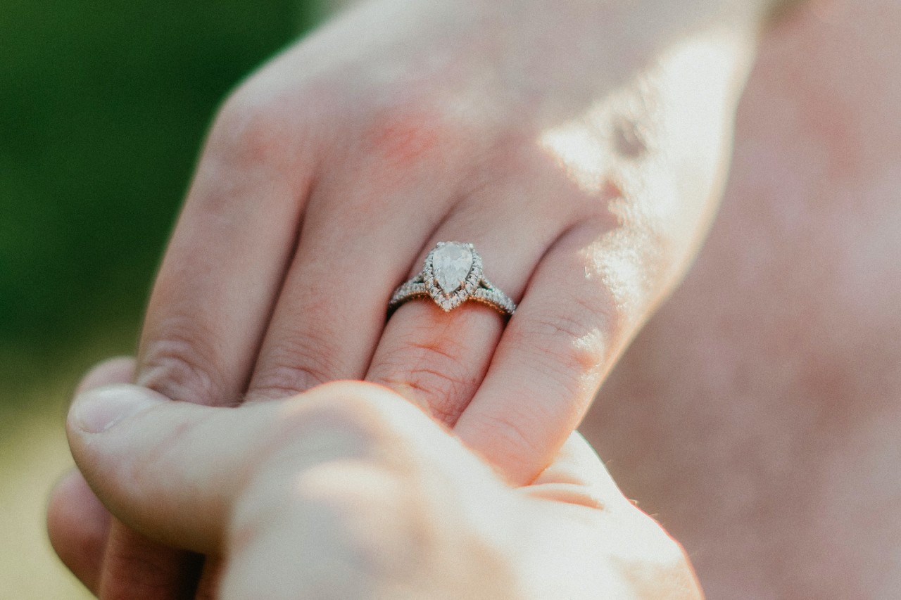 a person’s hand being held by another’s and wearing a pear shape halo engagement ring