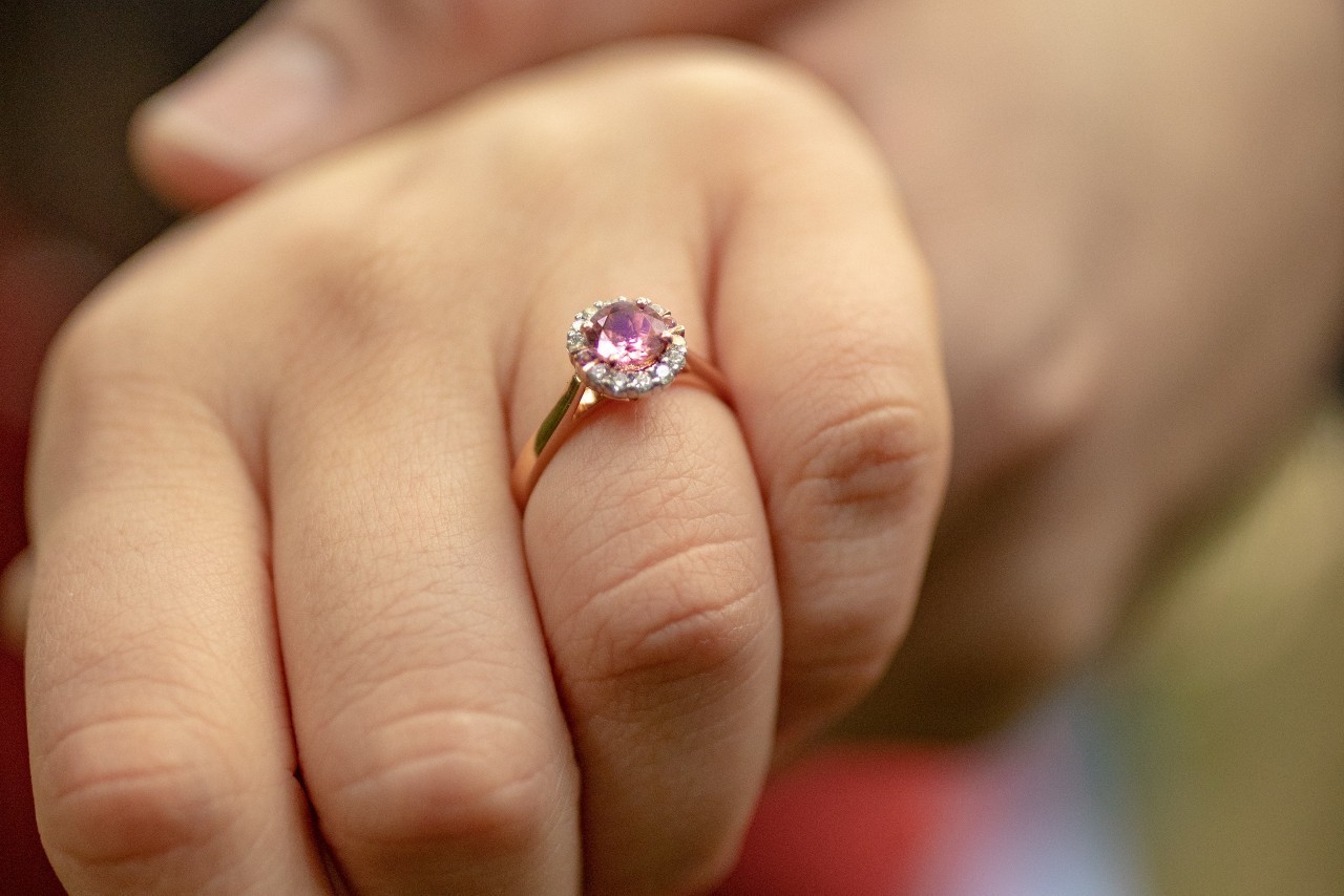 close up image of a hand donning a rose gold halo engagement ring with a purple center stone
