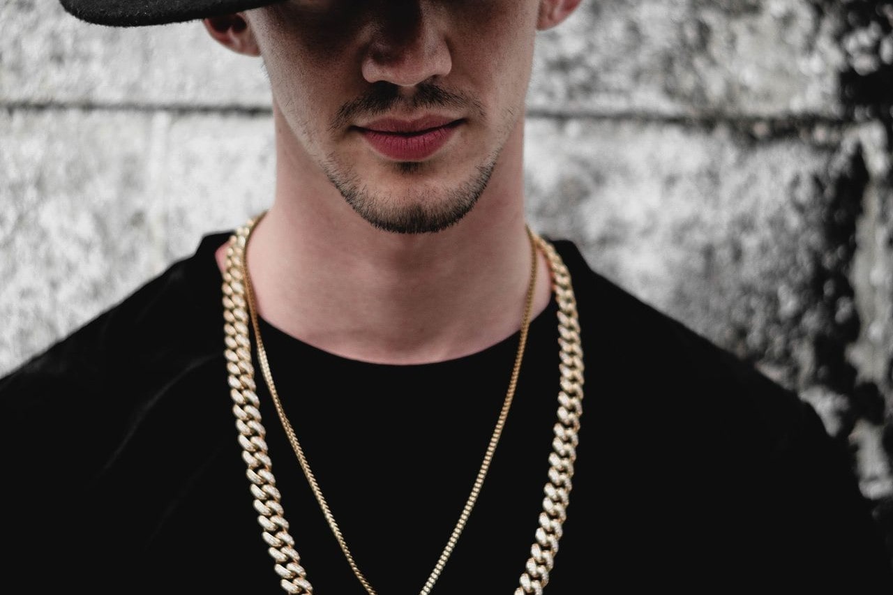 A man wearing two gold necklaces with a casual black tee.