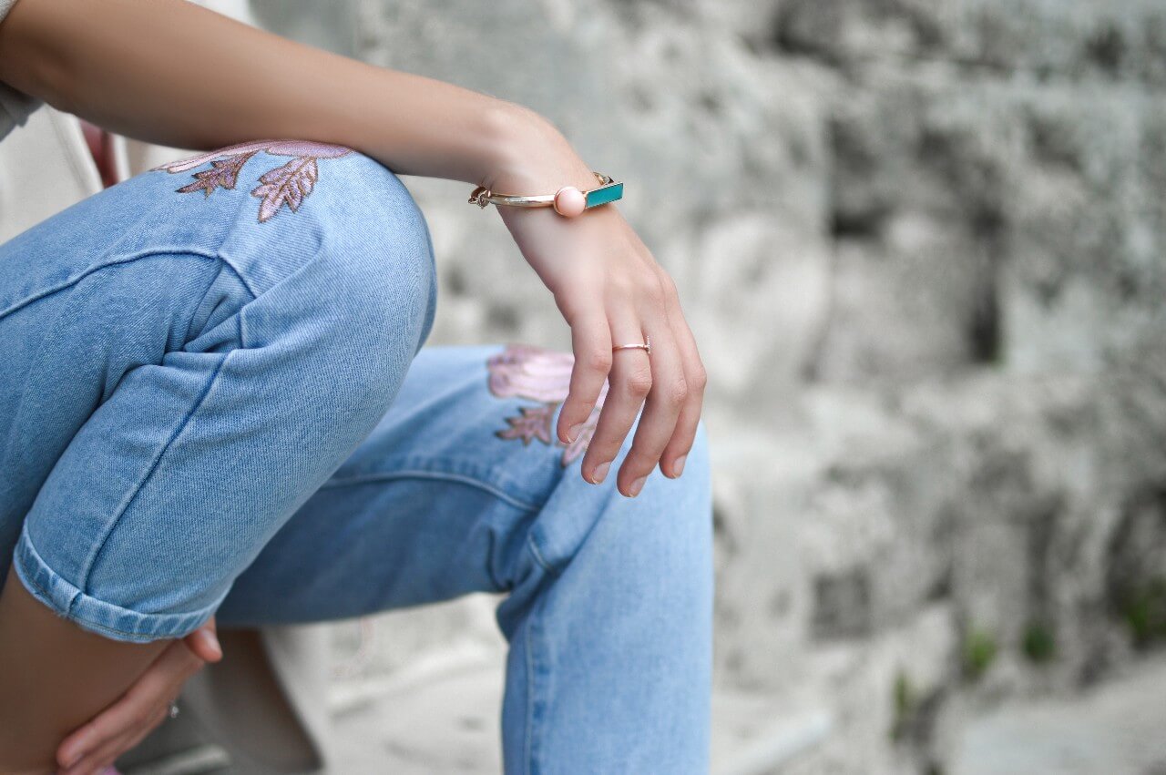 A woman in floral jeans wears a white gold gemstone bangle.