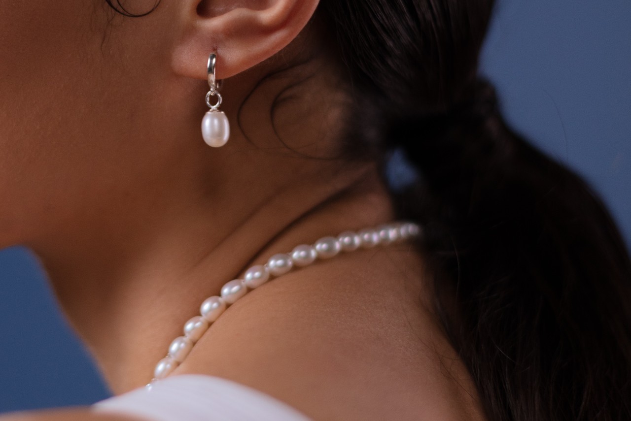 Close up image of a woman wearing a pearl necklace and pearl earring