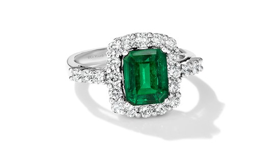 Silver ring inlaid with a large emerald surrounded by diamond accent stones