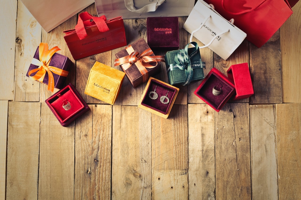 A variety of jewelry gifts, some wrapped, some open, sit on a rustic wooden floor during the daytime