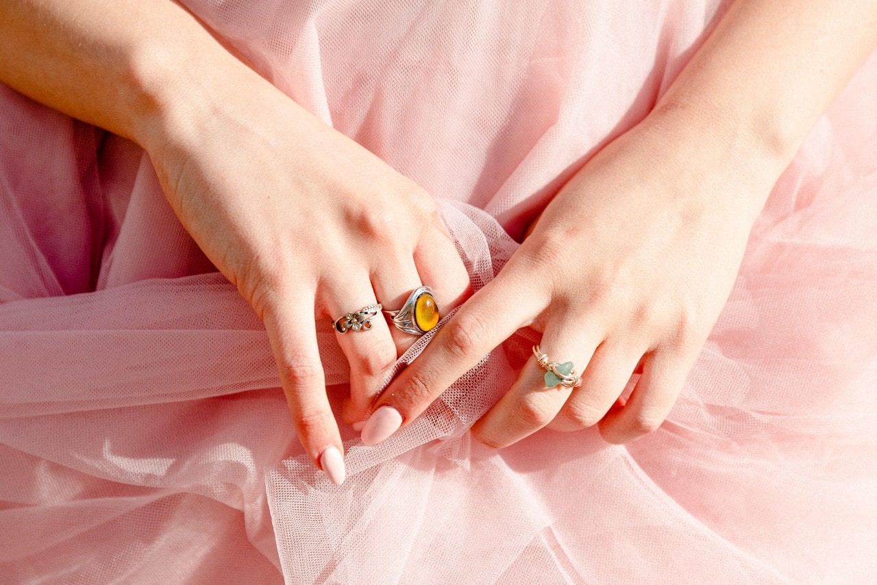 A woman wearing a pink tulle skirt lays her hands in her lap to show off three unique gemstone fashion rings