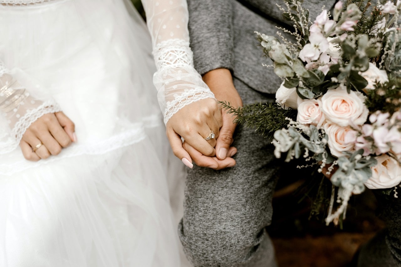 A bride and groom holding hands and an engagement ring visible