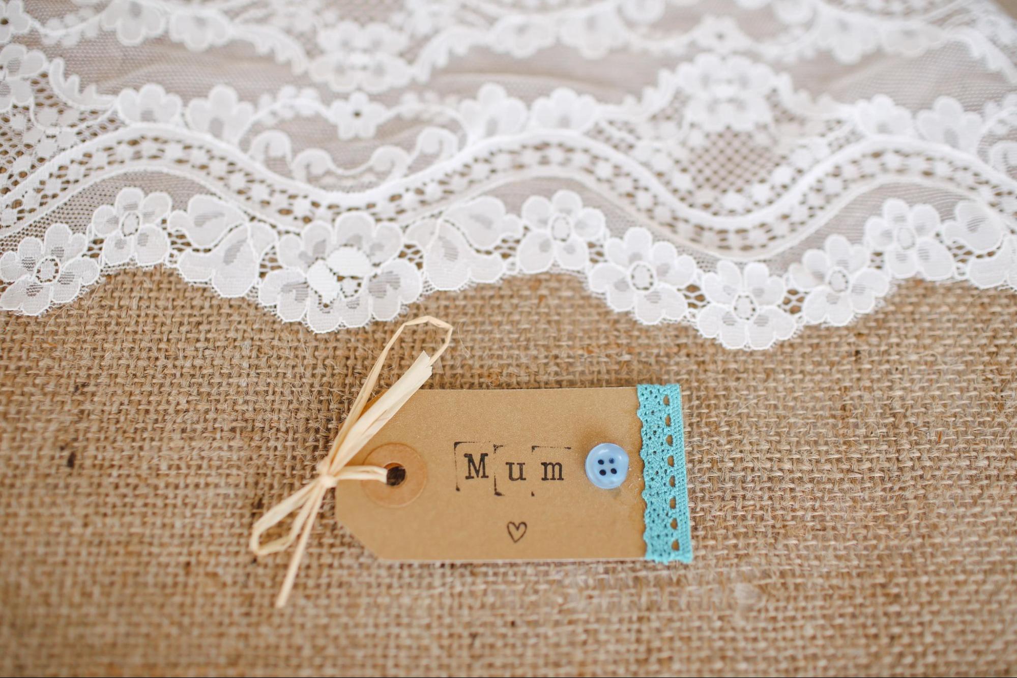 A homemade gift tag for a mother sits on a burlap table runner