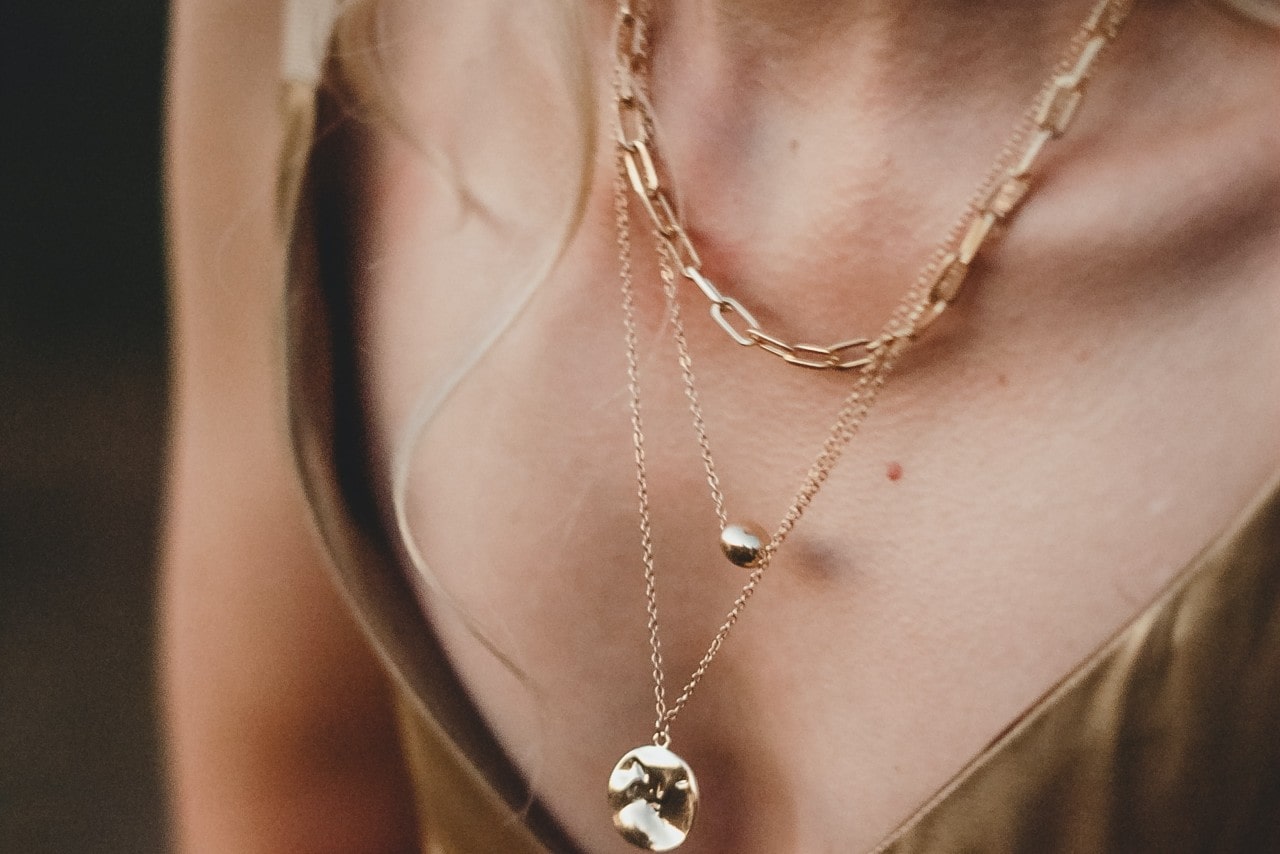 Close-up image of a woman wearing three layered gold necklaces