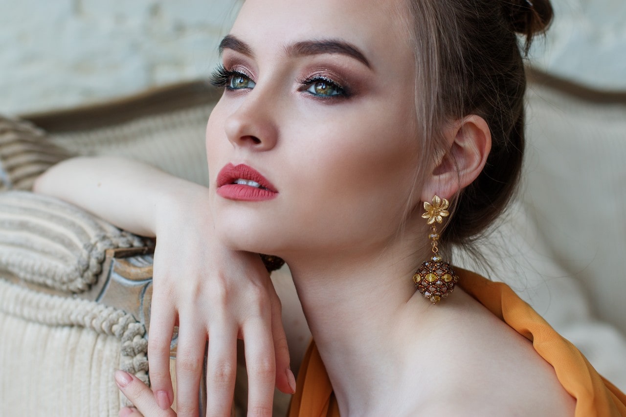 A fashionable woman wearing a dramatic drop earring and an updo leans against a couch