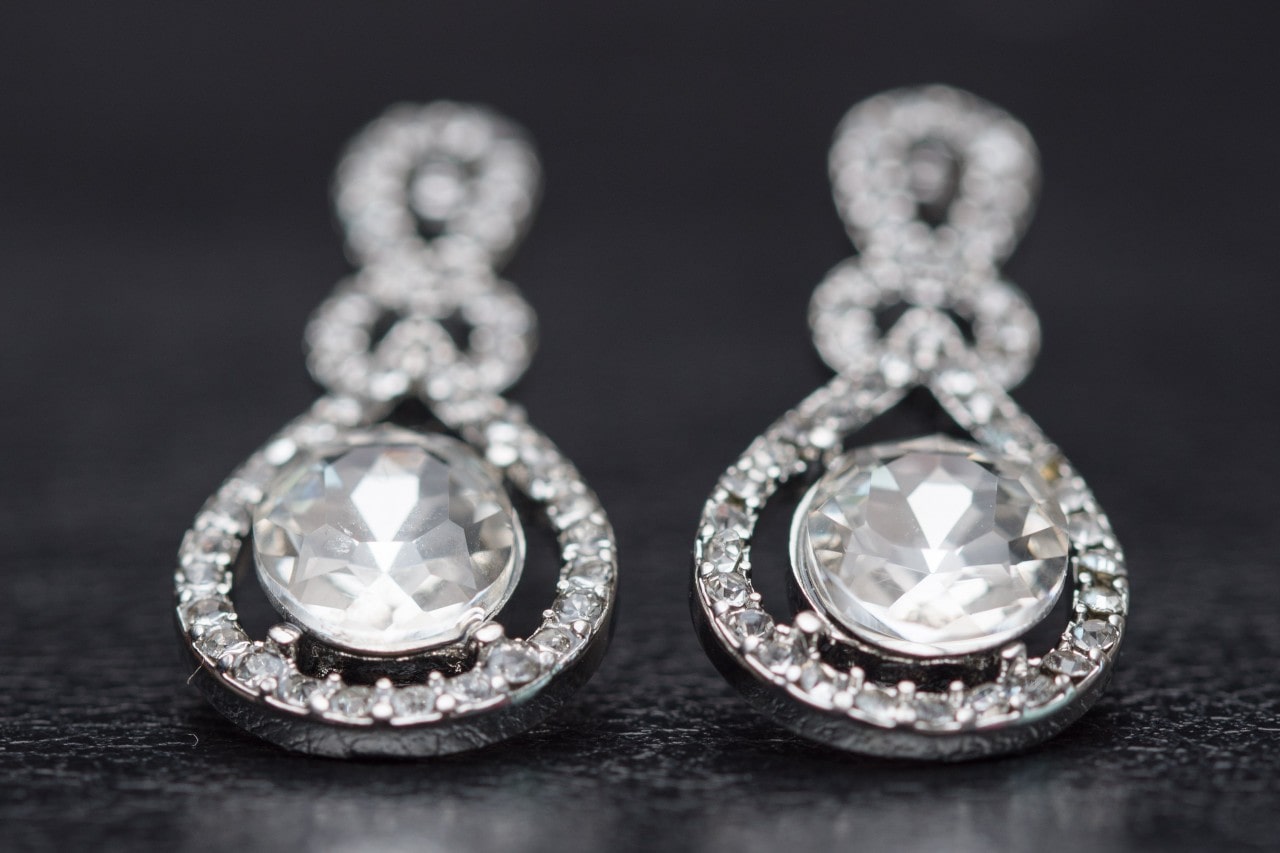 A pair of diamond drop earrings sit on a black table
