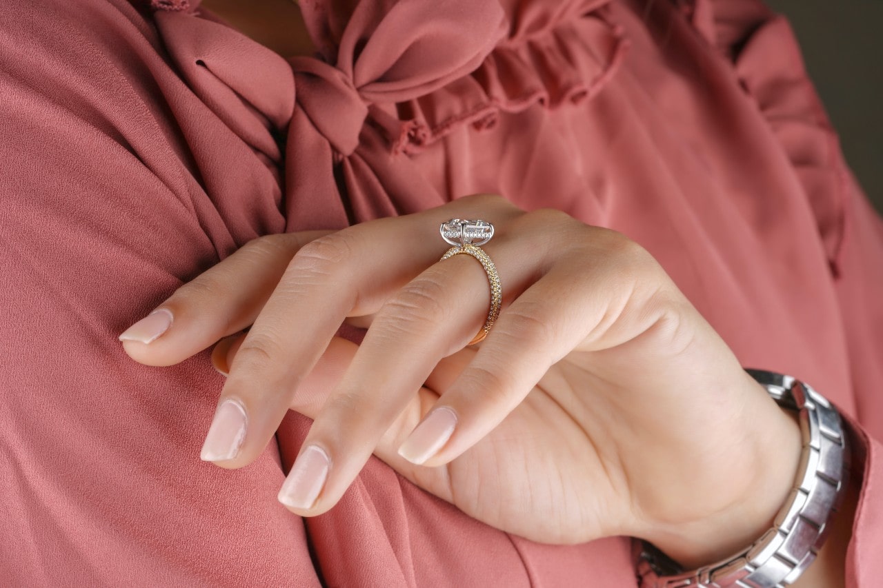 A woman in a pink blouse wearing a silver watch and a gold engagement ring