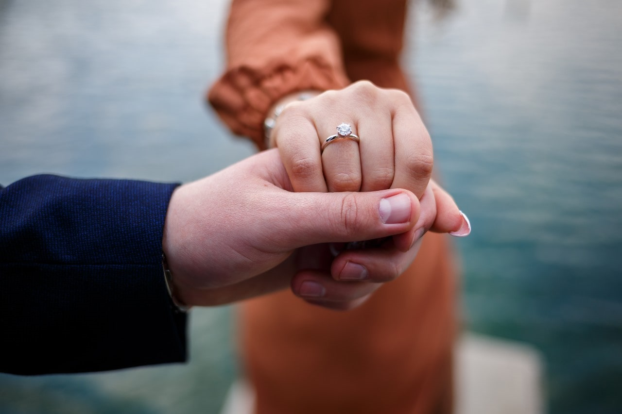 A man holding a woman’s hand, who is wearing an engagement ring