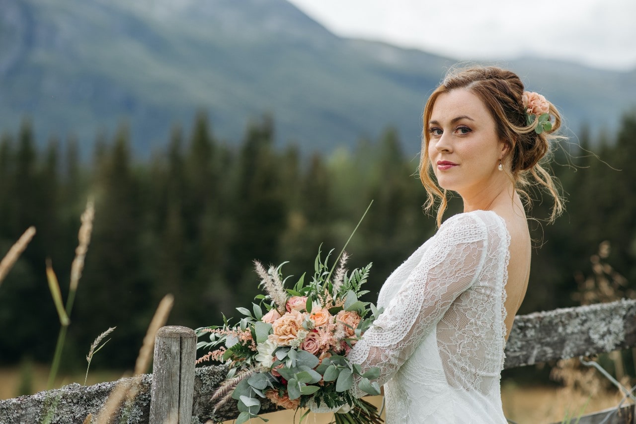 A bride leans on a wooden fence through a mountain.