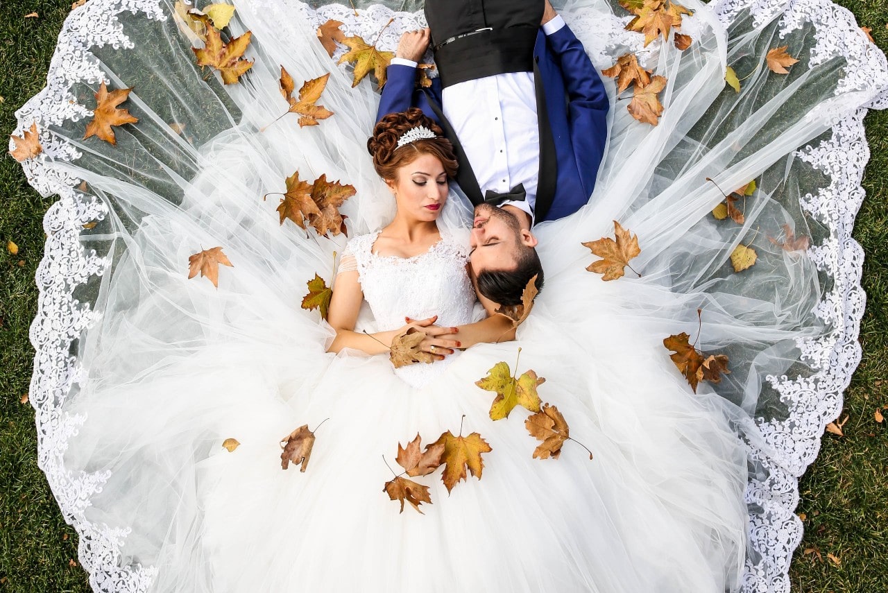 a bride and groom laying in the grass, covered in fall leaves