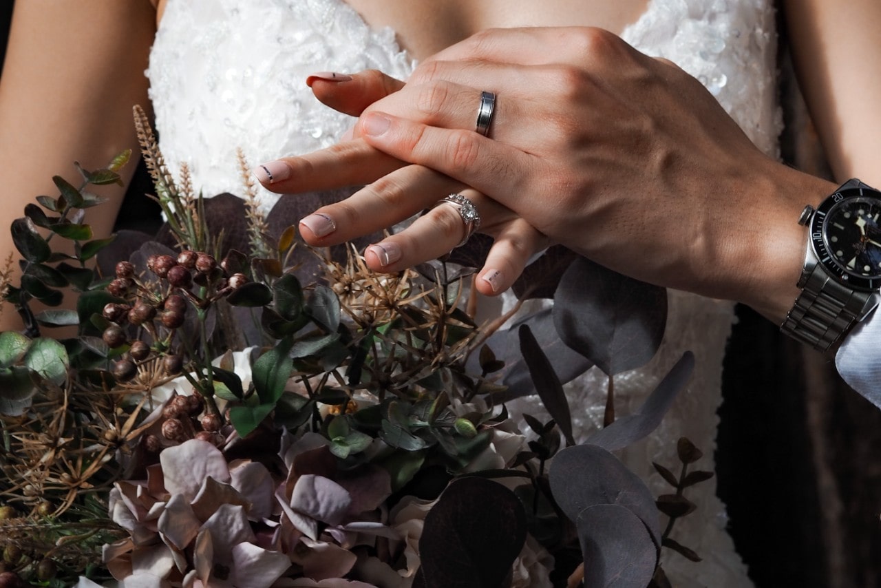 a bride and groom showing off their wedding bands and her fall-inspired bouquet