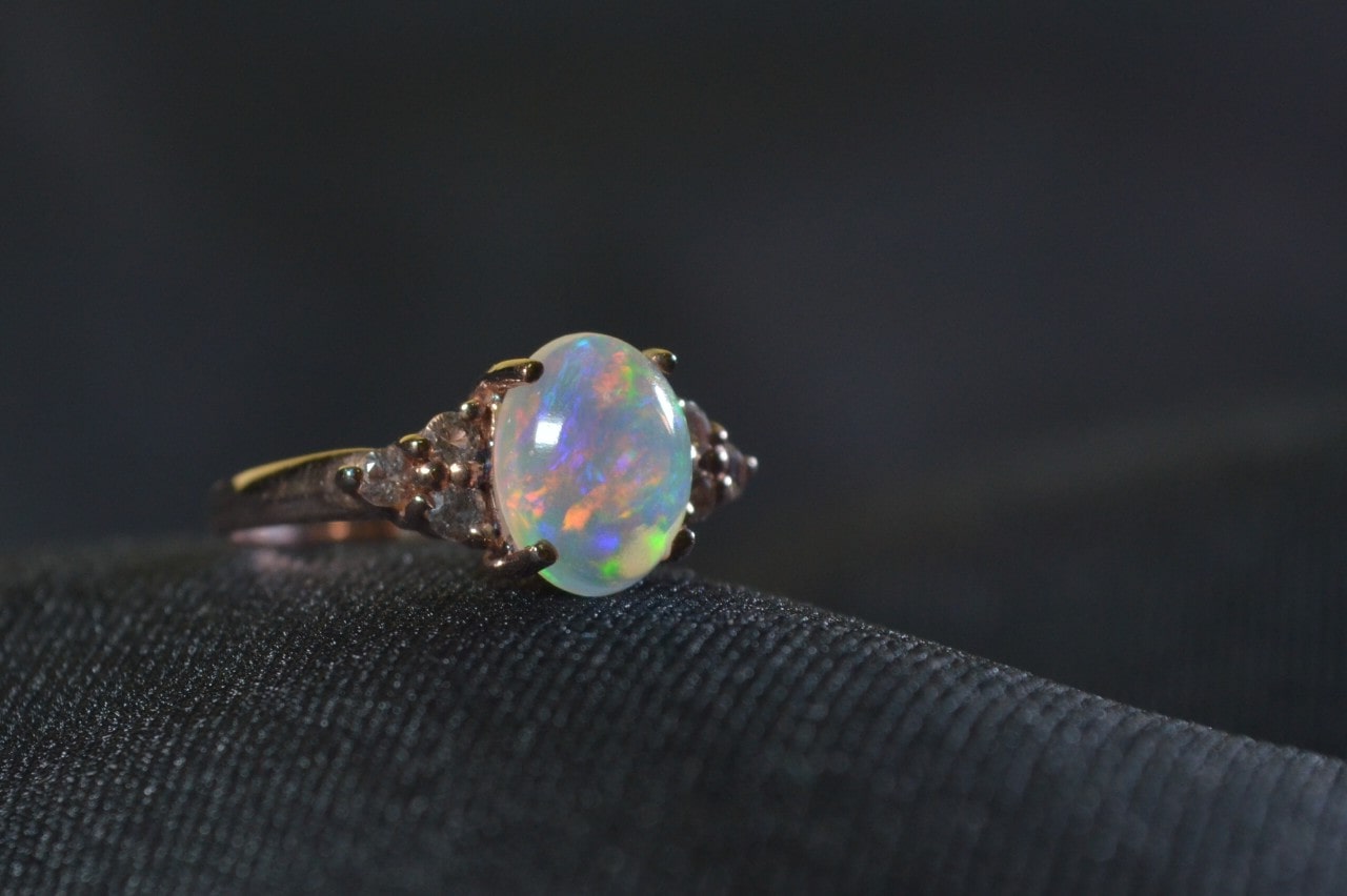 A yellow gold, oval-cut opal fashion ring sits on a black fabric.