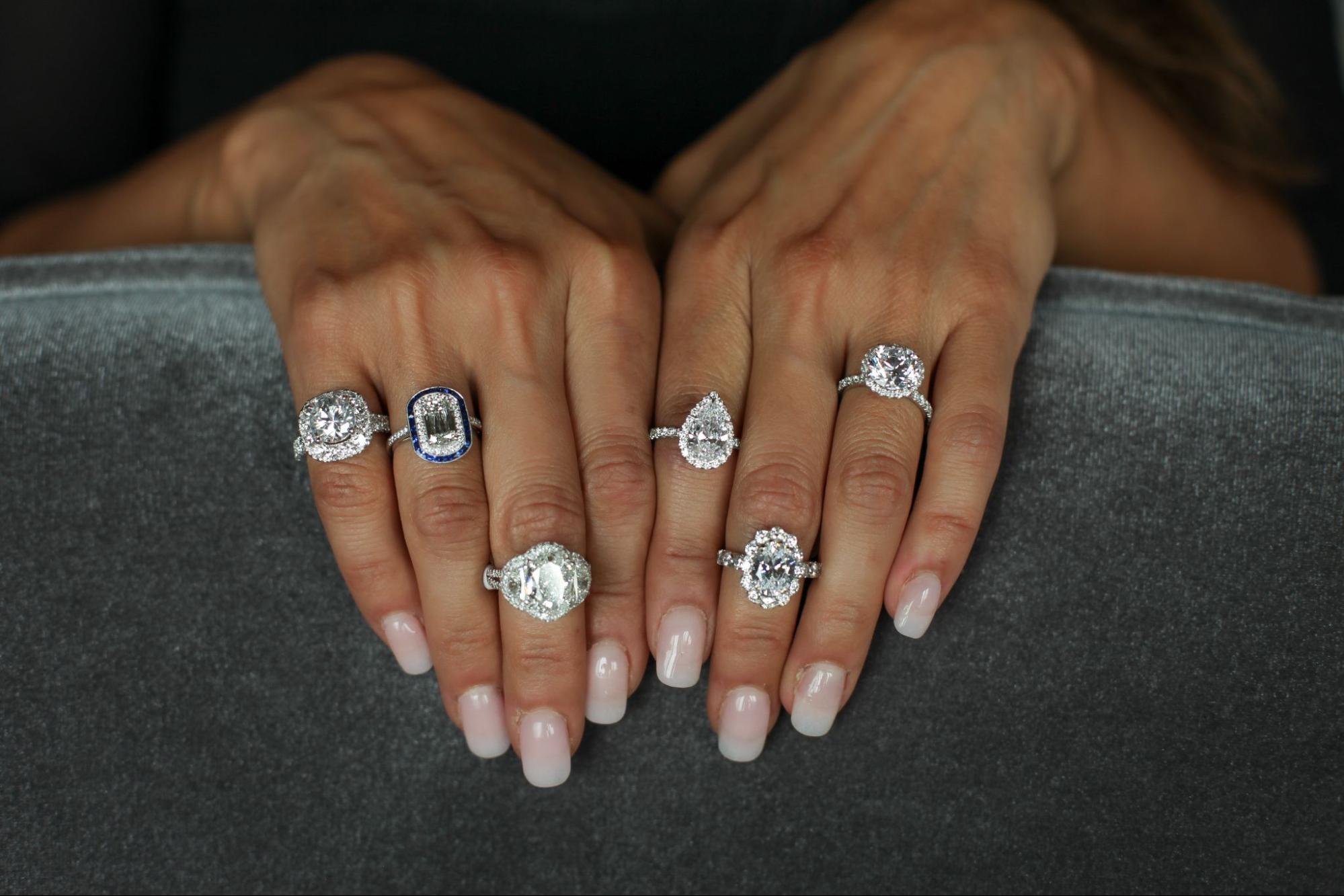a woman’s hands with multiple diamond rings on almost every finger