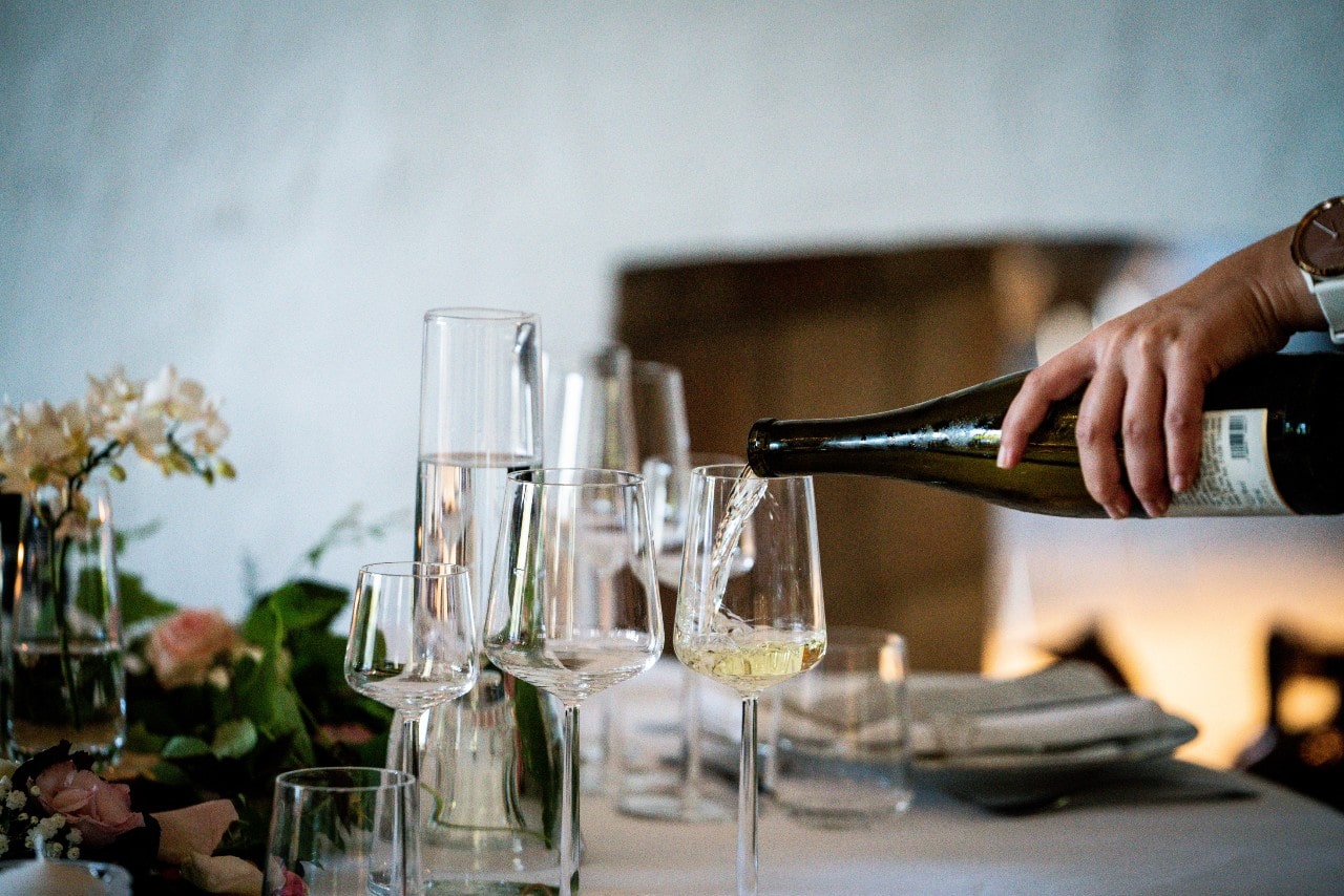 A woman pours champagne in an array of glasses at a dinner table.