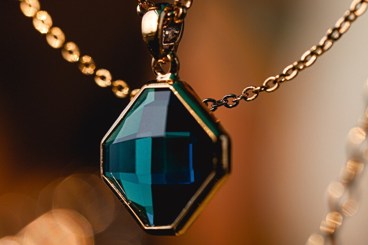 close up image of a gold necklace featuring a blue gemstone pendant