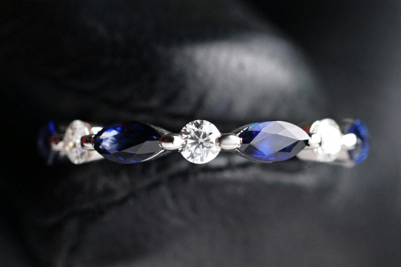 close up image of a diamond and sapphire wedding band held by a gloved hand
