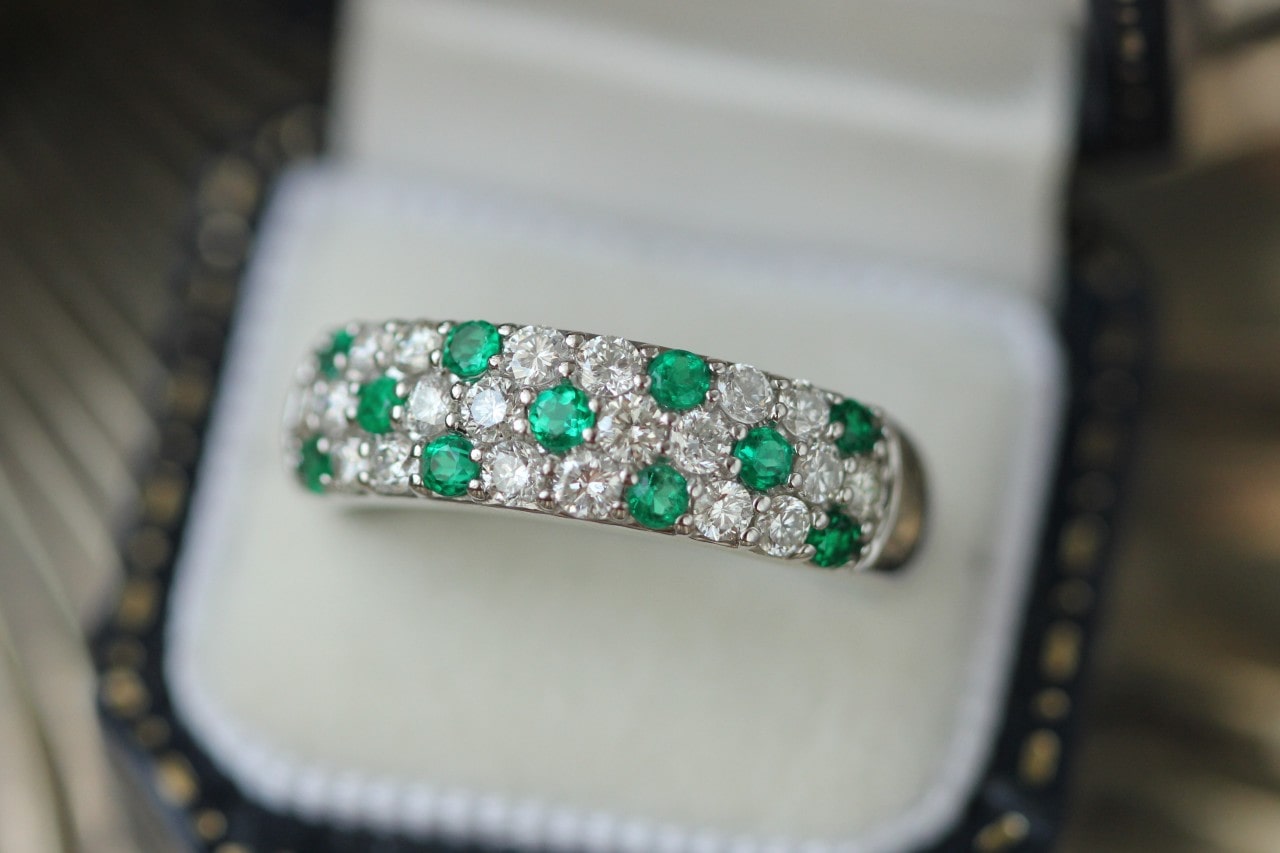 a pave set wedding band featuring diamonds and emeralds in a white ring box