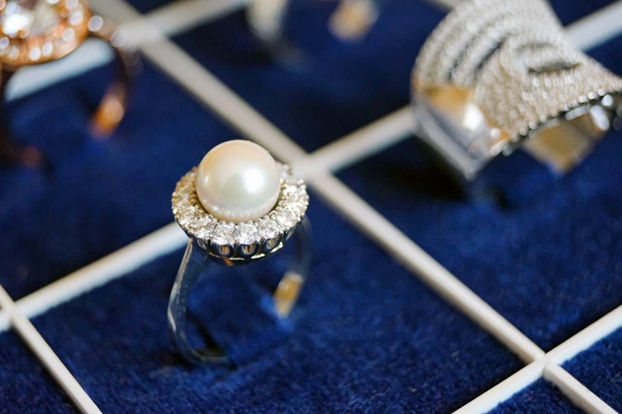 a white gold fashion ring featuring a large pearl and a diamond halo in a blue velvet jewelry box