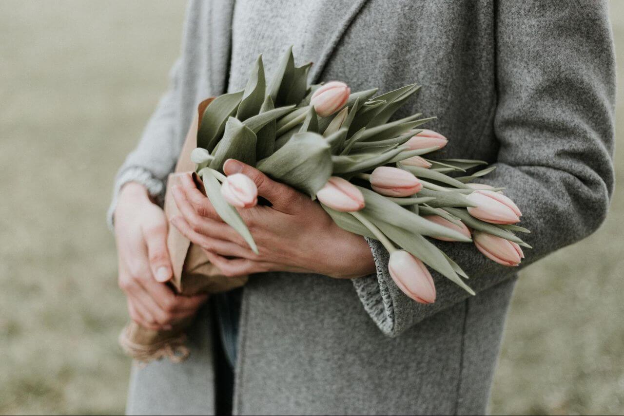 A mother wearing a gray cardigan holds a bouquet of pink tulips.