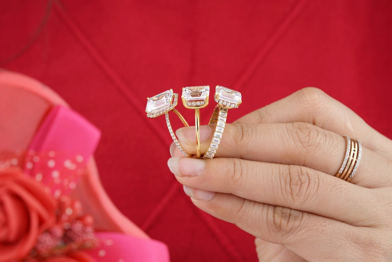 a lady’s hand holding three custom-designed engagement rings on a red background